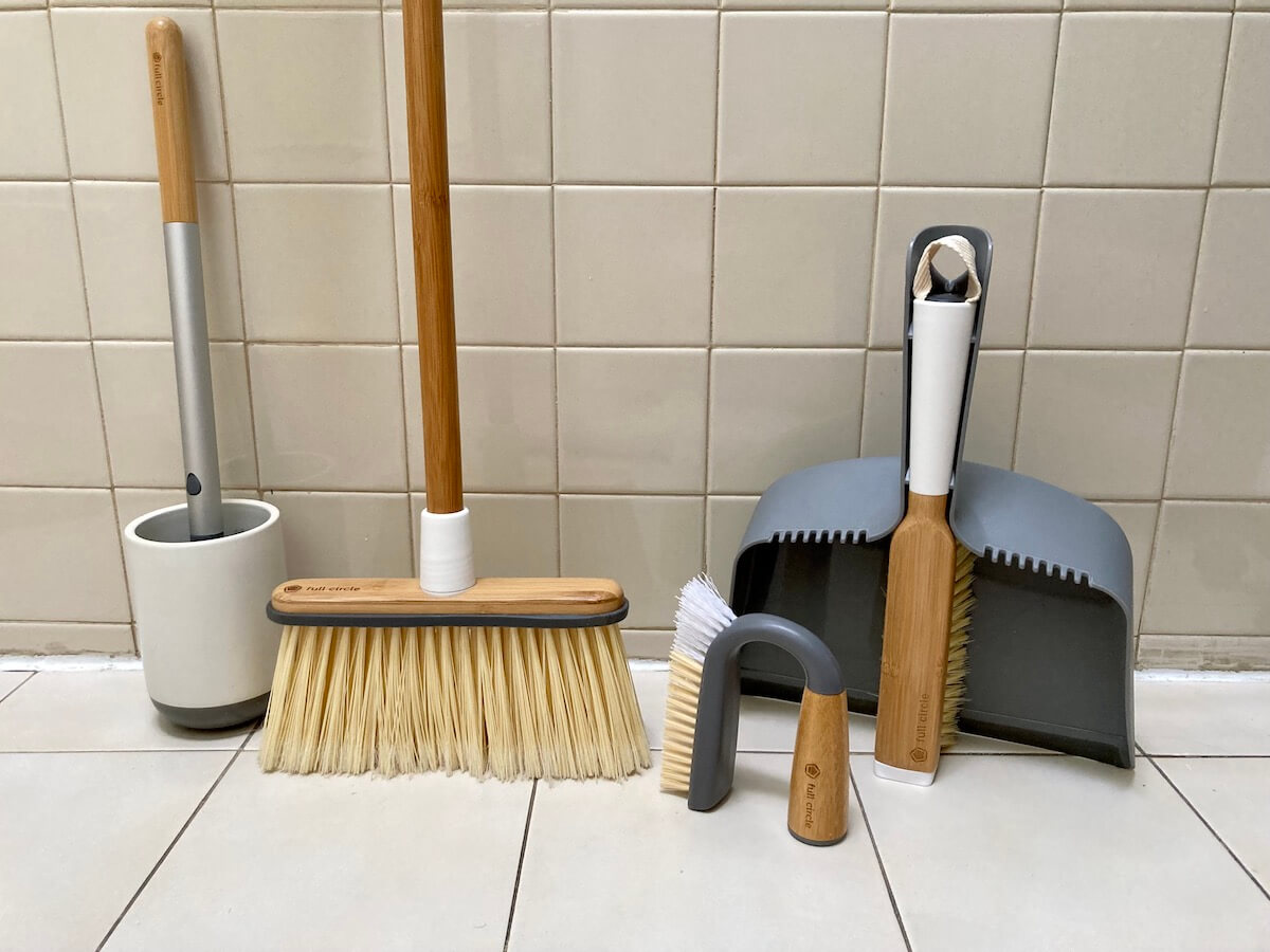 Four Full Circle products: toilet brush, broom, group and tile brush, and dustpan with brush. They are displayed against a beige tiled wall.