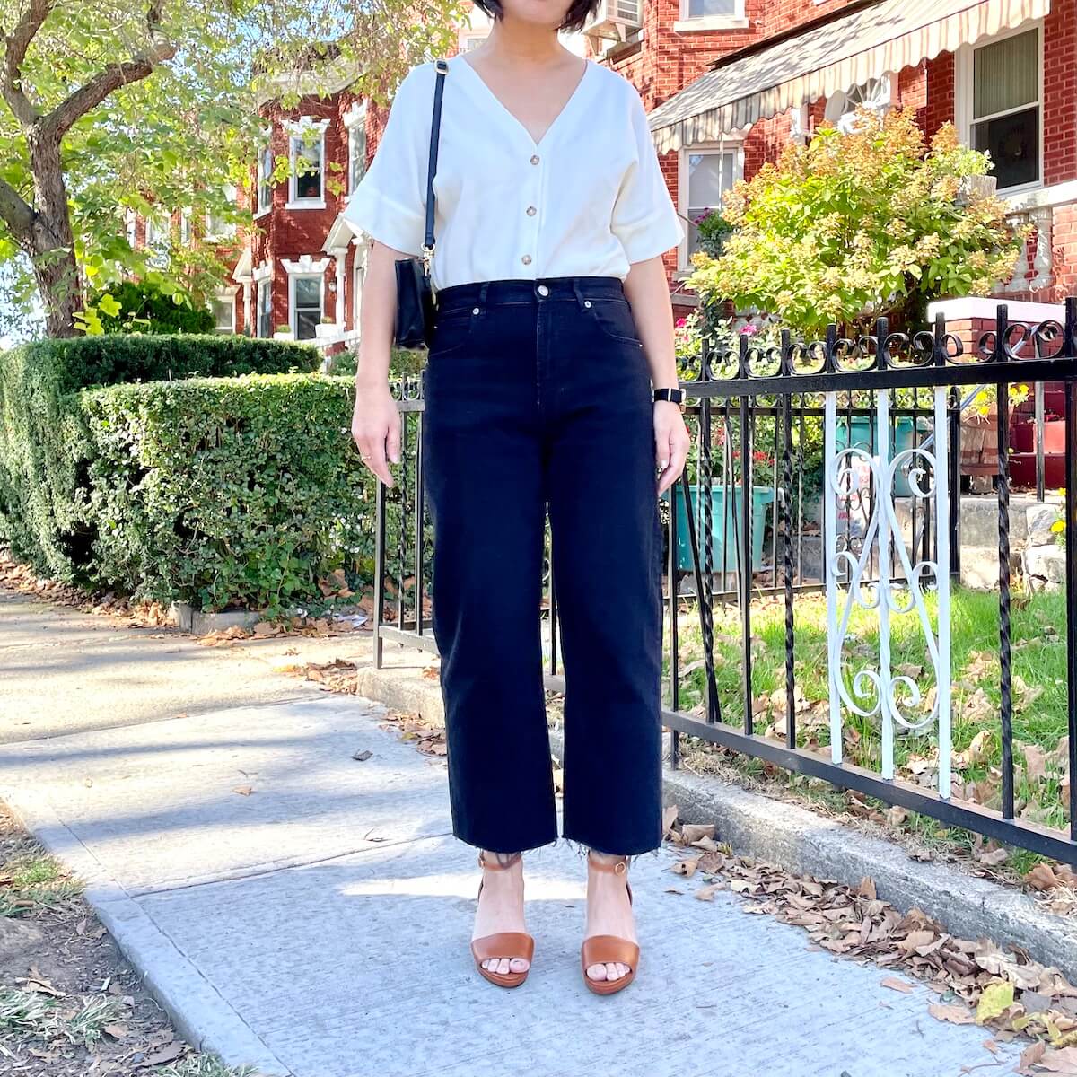 Me, a person with short black hair, standing outside wearing the Everlane Way-High Jean with sandals. There are red brick homes in the background.