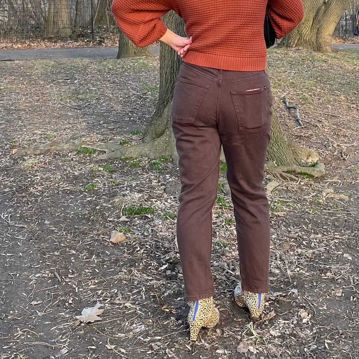 Everlane Cheeky Jean in brown, worn by a person with leopard print boots, from the back. There is a phone in one back pocket.