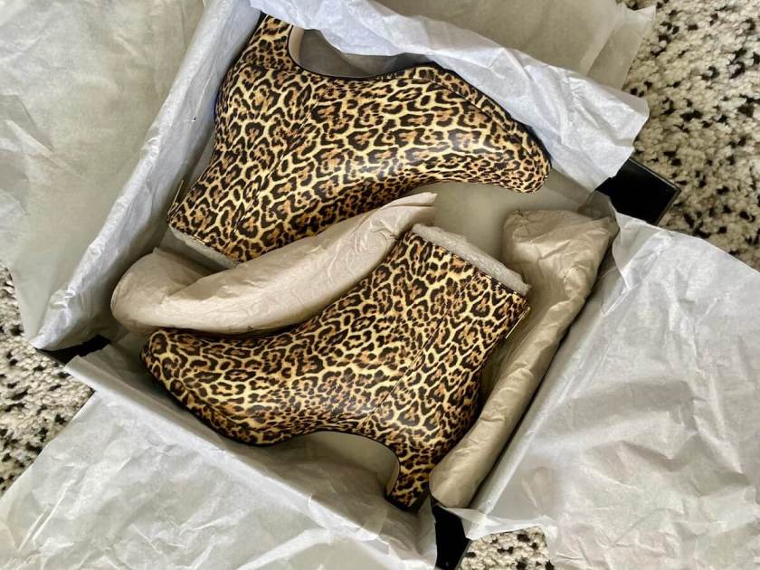 A shoe box open to show leopard print ankle boots packaged in paper.