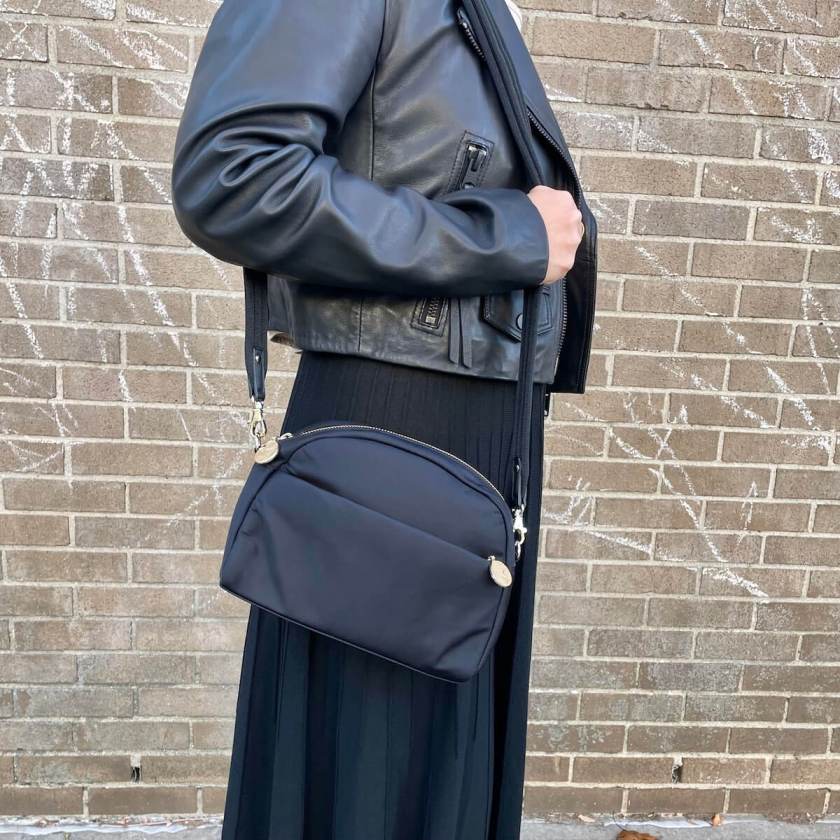 A closeup of a dome-shaped purse worn by a person who is also wearing a black motorcycle jacket.