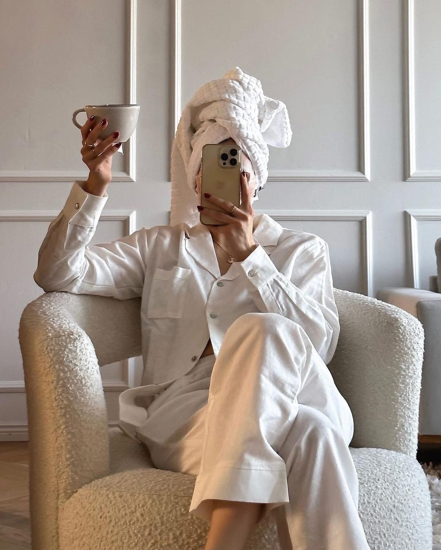 The ultimate Sunday reset routine. Sunday self-care checklist ideas and tips to prepare and recharge for the week. Things to do on Sunday. What to do on Sunday. weekly reset routine. Woman holding a cup wearing a white pyjama set and a white towel wrapped around her head with the phone covering her face to take a selfie.