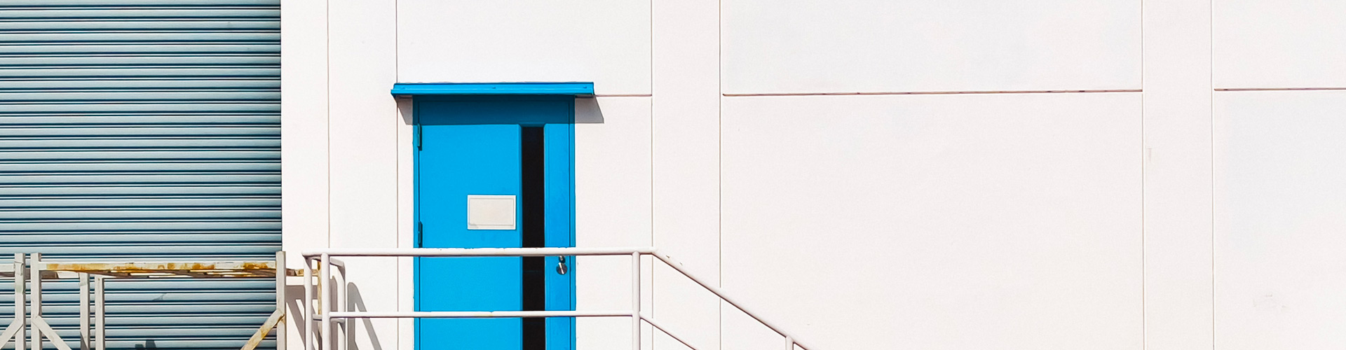 warehouse with white wall, gray garage door and blue doors with staircase
