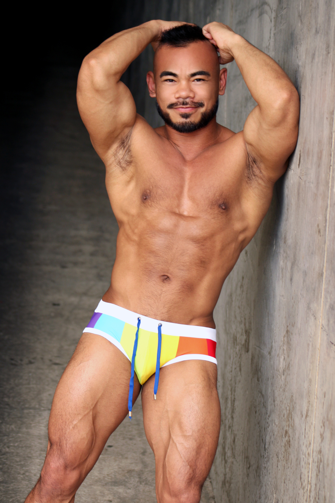 Jason Luna, bearded, shows off his muscles in rainbow swimming briefs 