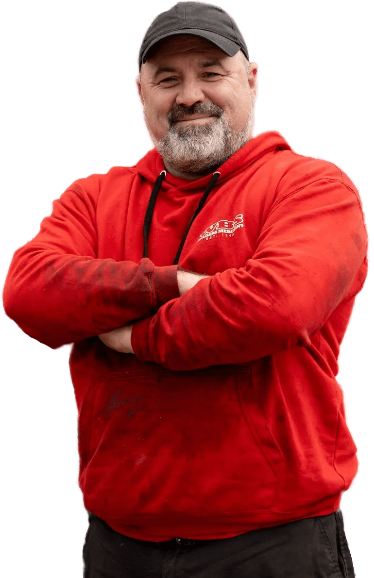 Man in a red hoodie and black cap stands with arms crossed, smiling at the camera.