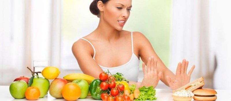 A woman raises her hands in front of a table abundant with fresh fruits and vegetables, symbolizing healthy diet and hydration.