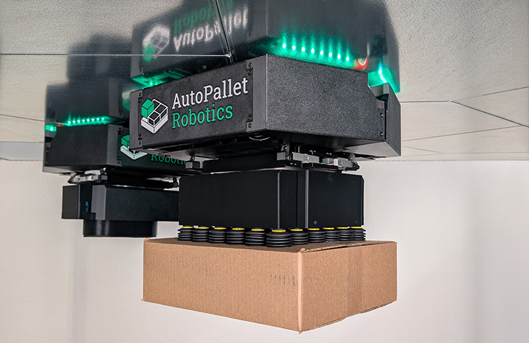 The AutoPallet system uses small ceiling-mounted robots that use powerful magnets to drive upside-down on steel panels mounted overhead and reach down to pick and place cases on pallets and conveyors below.