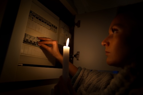 Woman in total darkness investigating fuse box at home during power outage or blackout