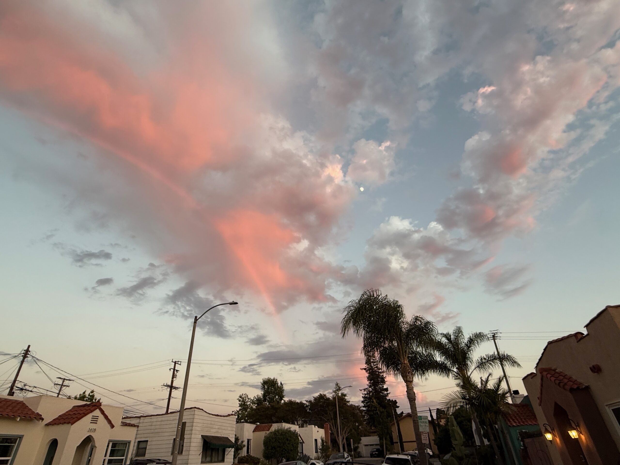 Confluence of sunset clouds, rainbow, and full moon over a small Spanish revival neighborhood.