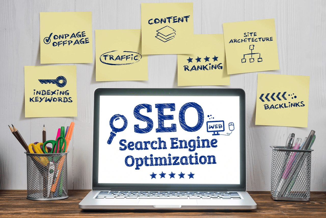 Laptop with SEO (Search Engine Optimization) on the screen surrounded by sticky notes with keywords like content, backlinks, ranking, and traffic.