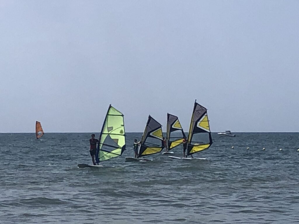 Grupo de niños que siguen al monitor navegando en la clase de windsurf