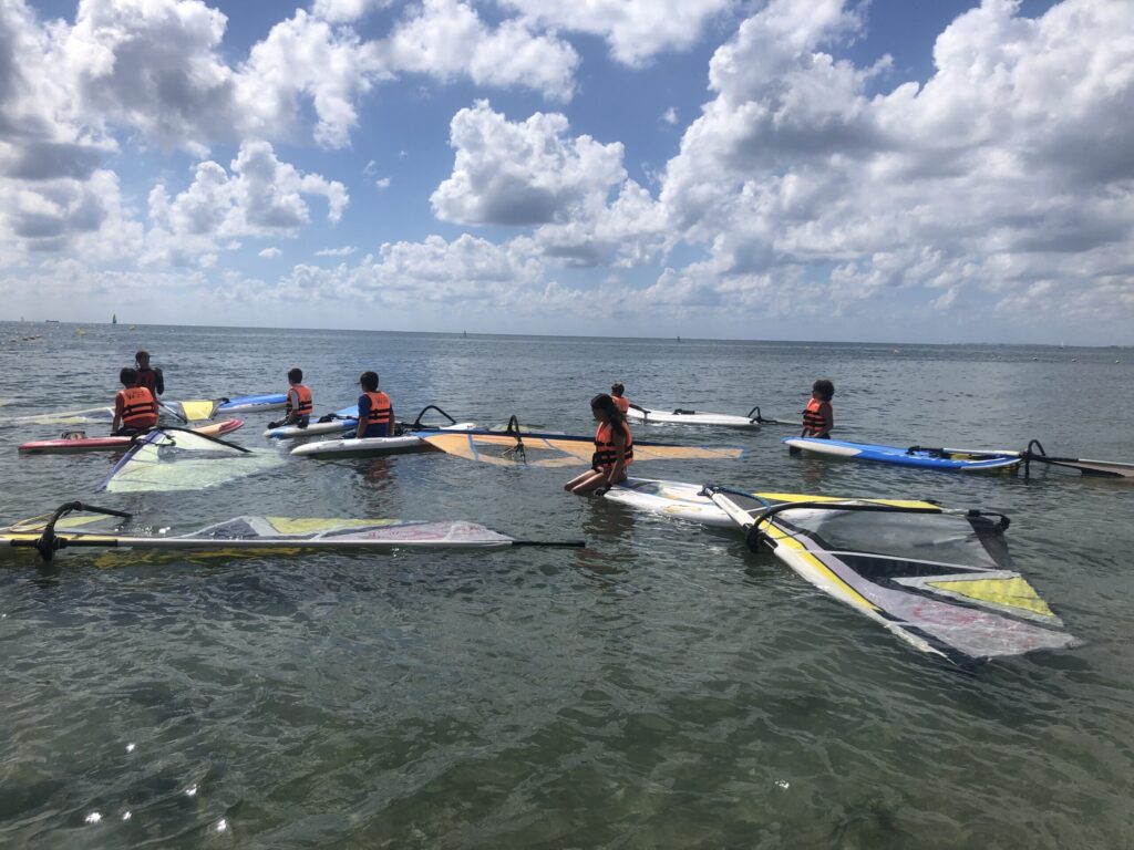 Grupo de niños escuchando la explicación de la monitora antes de comenzar la clase de windsurf