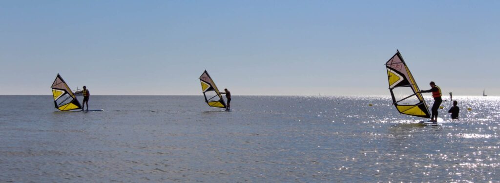 Tres personas aprendiendo windsurf en un mar calmo