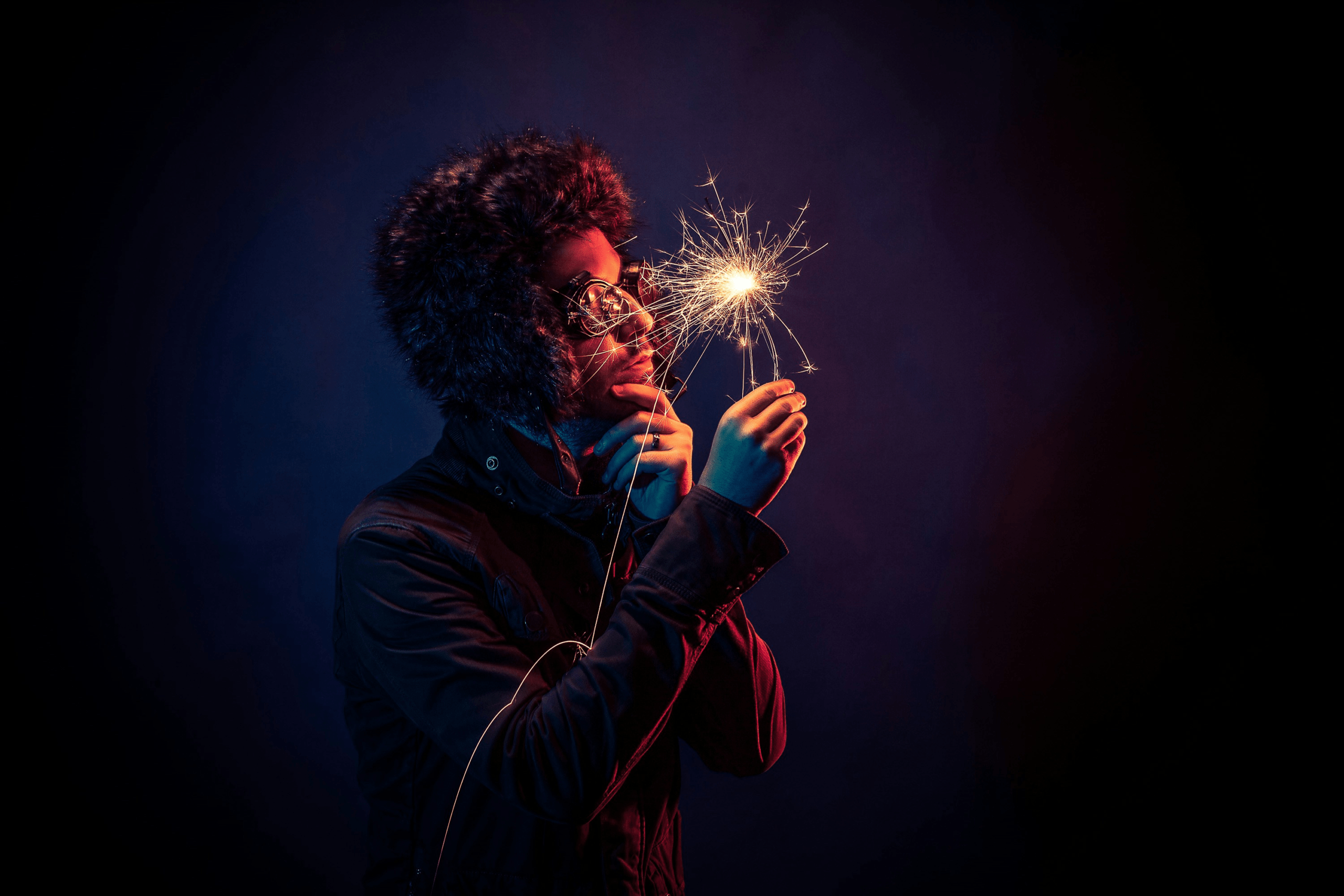 An image of a man in an insulated hat looking inquisitively at a sparkler.