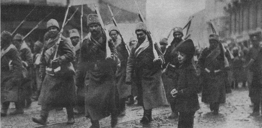 A black and white photo shows a group of soldiers marching with rifles over their shoulders, wearing long coats and hats, while a young child walks alongside them on a city street.