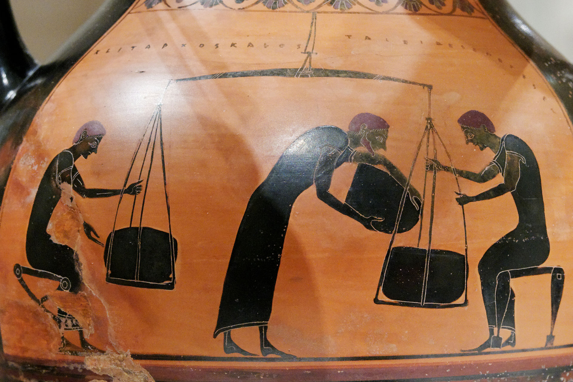 Ancient Greek pottery showing three figures weighing sacks on a large balance scale; two kneel on either side while a third, in the center, bends over to inspect the balance.