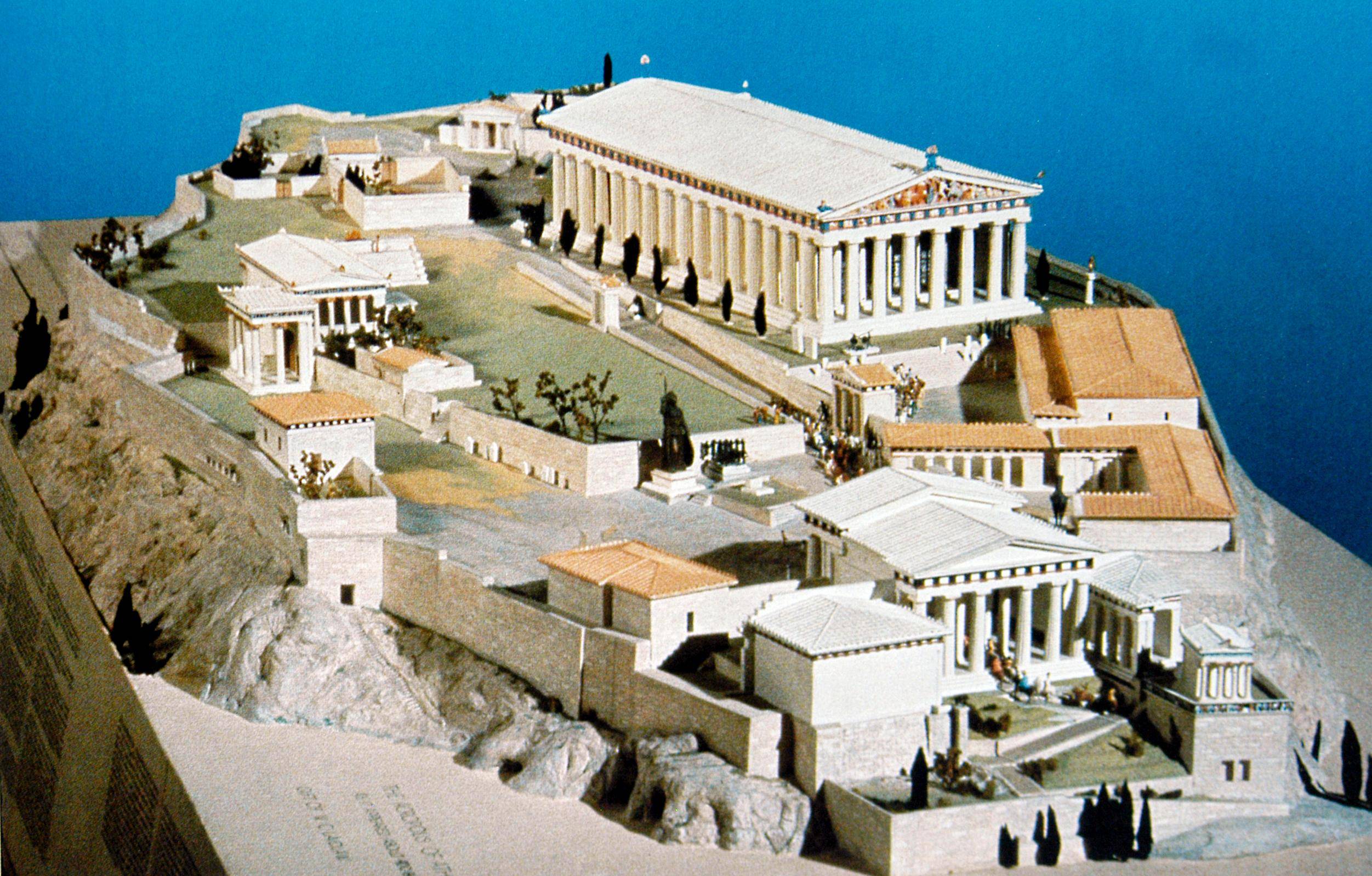 A detailed model of the ancient Acropolis of Athens, featuring the Parthenon and several other classical Greek buildings on a rocky hilltop, set against a blue background.