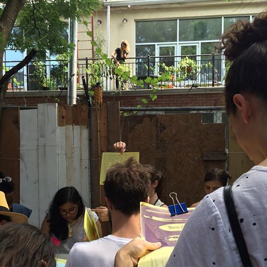 Book binding class at the Bushwick Art Book & Zine Fair 2016. July 2016. Photo by Michele Witchipoo. In the background behind the book binding class, you can see signs of the hyper gentrification happening all over NYC.