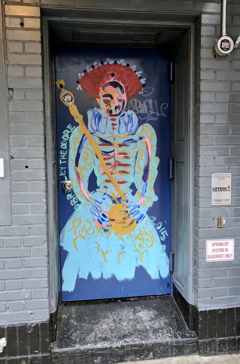A Bradley Theodore skeleton Queen in bold colors waits to receive you in the recessed door. Street art that survived.