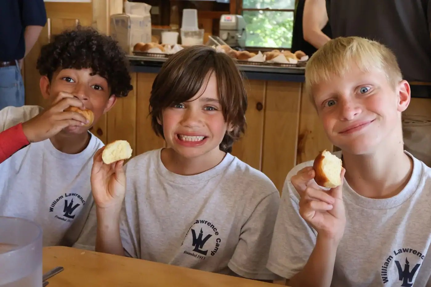 Three campers wearing William Lawrence Camp shirts enjoying rolls together in the dining hall
