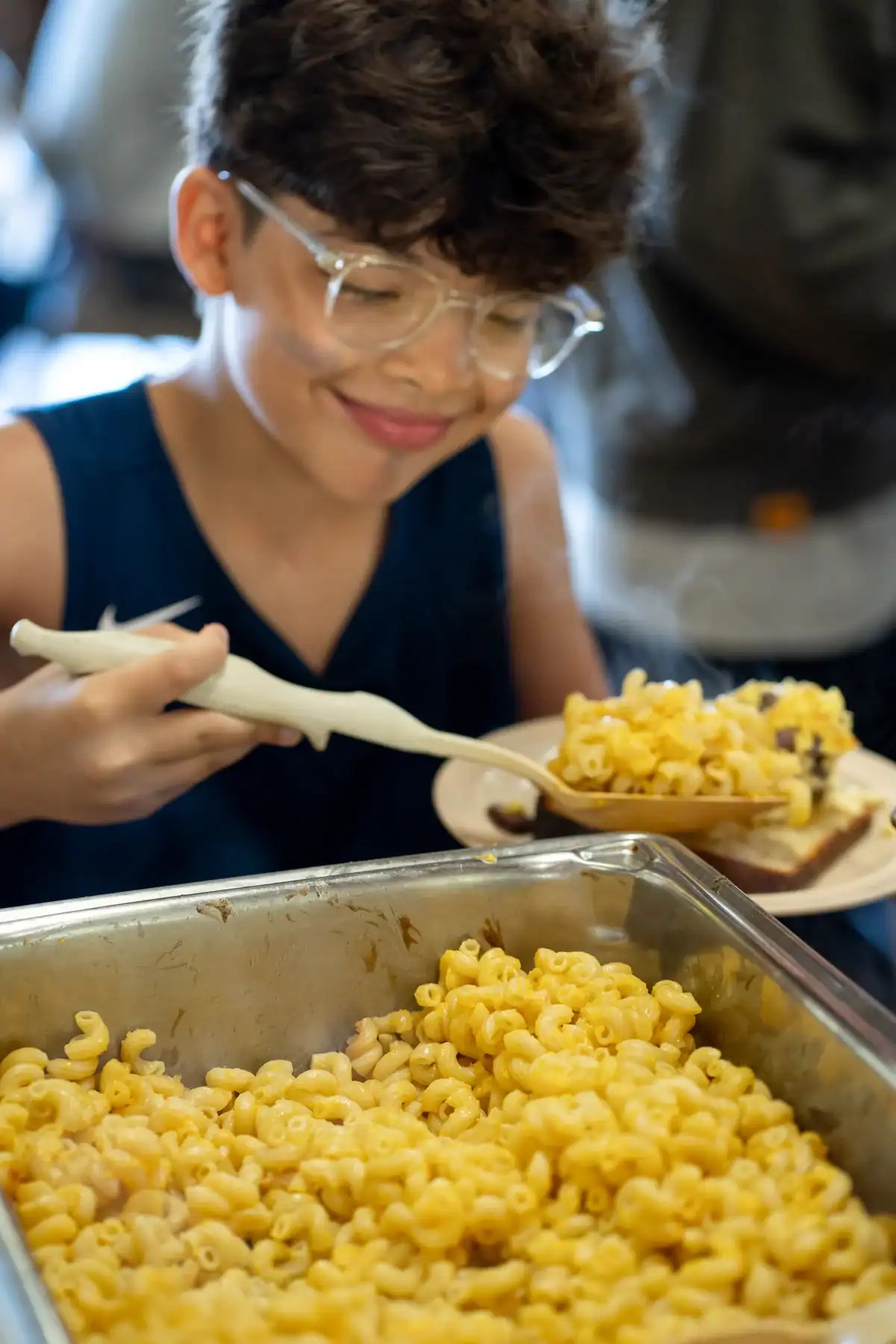 A smiling camper serving macaroni onto his plate