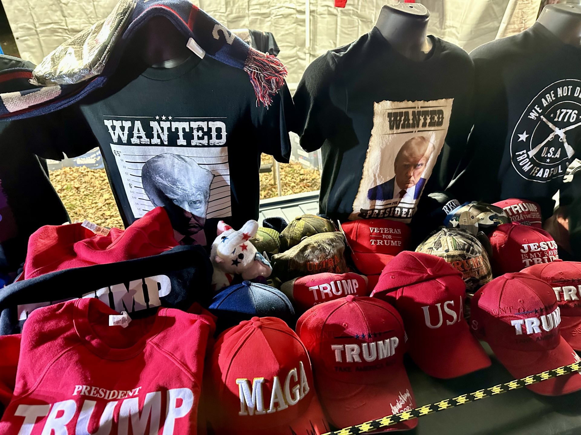 Trump and MAGA hats and shirts with posters and memorabilia displayed inside a tent.
