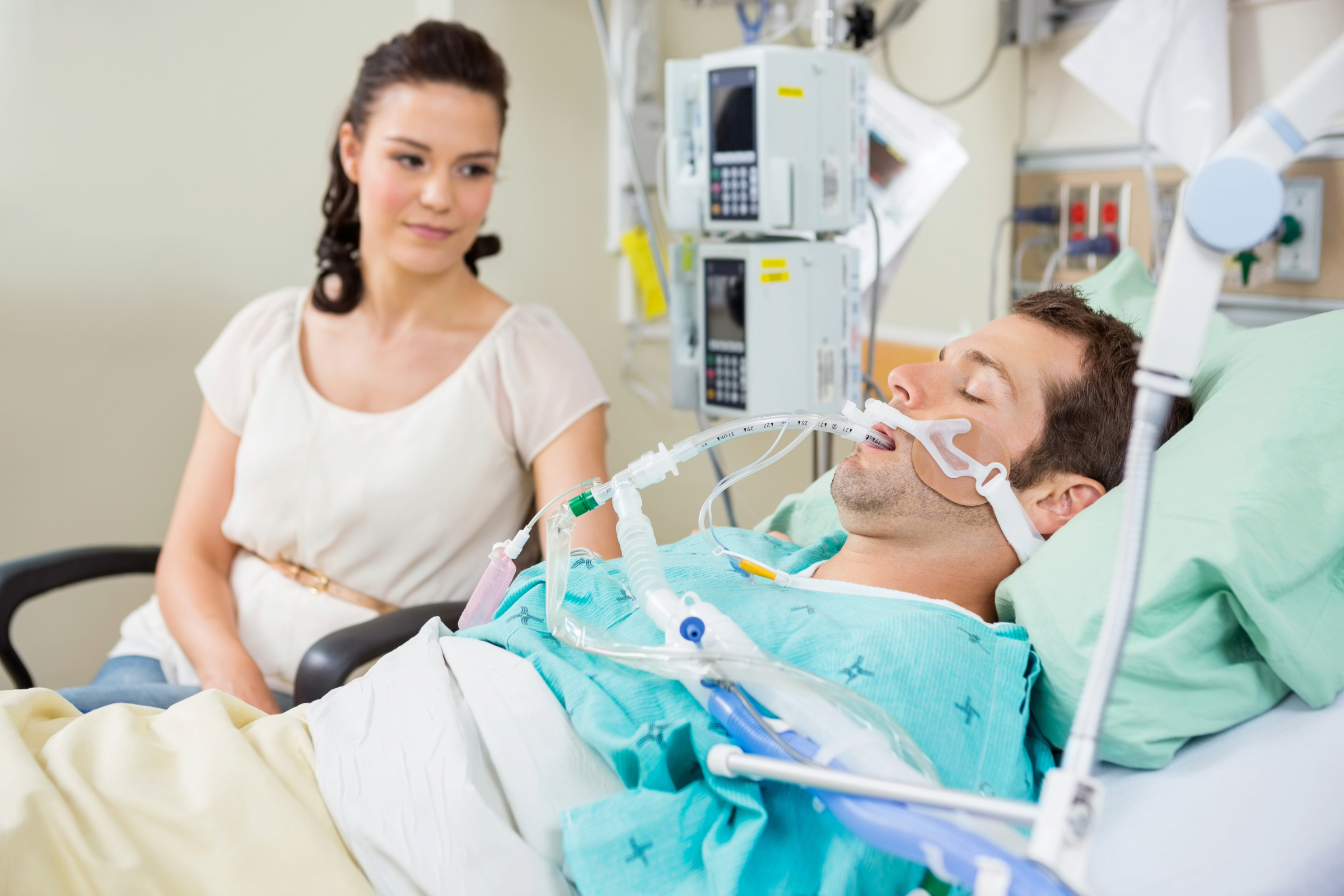 A woman sitting by a man's beside in the hospital.