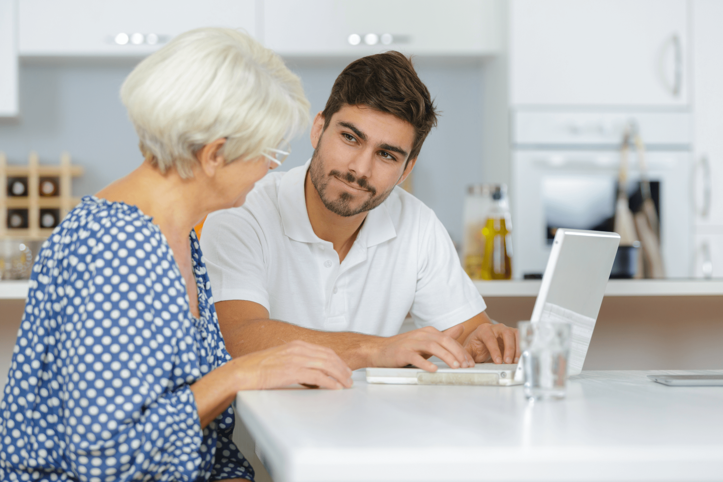 A man, sitting with a senior lady, helping her on her laptop.