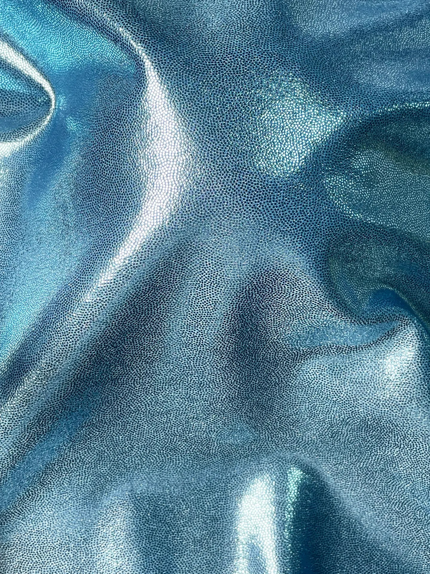 High-quality Korean mystique spandex fabric displaying a flawless liquid metallic shine under industrial spotlights