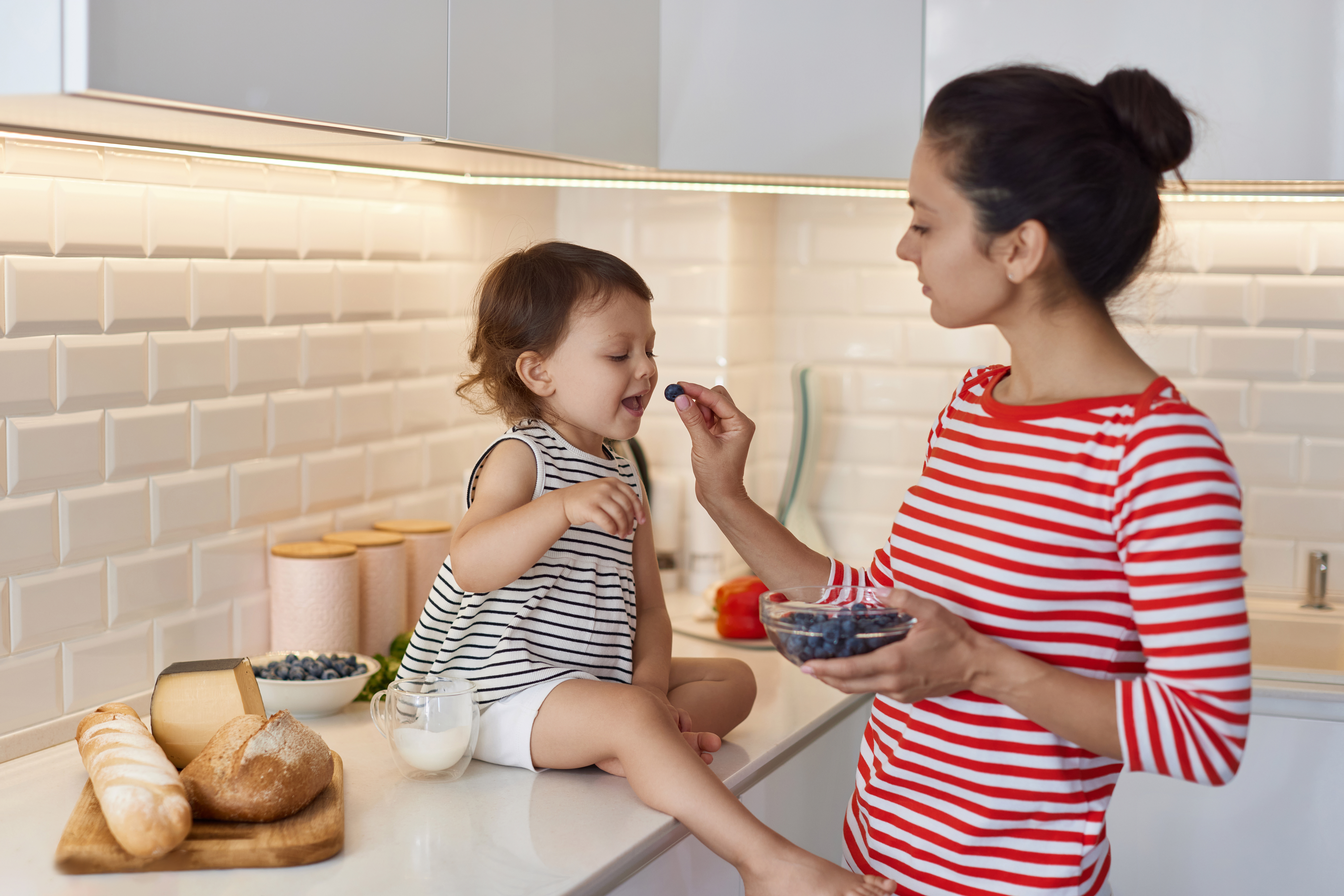 Discover the Incredible Health Benefits of Blueberries Blueberries. This is why you should eat them every day. Mother gives to the little baby girl fresh blueberries in white kitchen