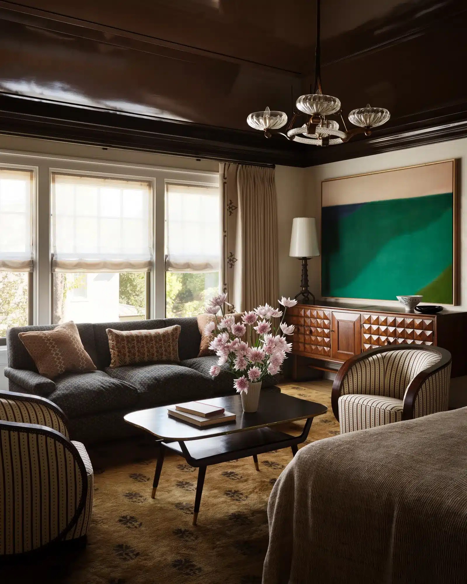 A colorful traditional living room featuring jewel-toned seating, antique furniture, framed artwork, patterned textiles and layered decorative accessories inside a beautifully restored historic home.