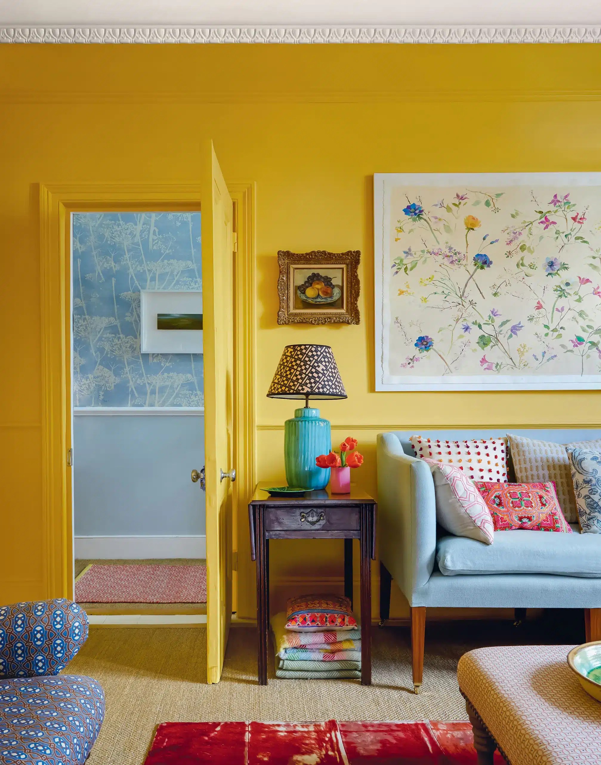 A colorful living room featuring soft pink walls, velvet armchairs, colorful cushions, framed artwork, layered textiles and decorative accessories in a stylish London townhouse.
