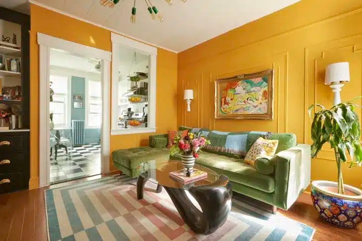 A colorful small living room featuring a blue sofa, a mustard yellow accent chair, a gallery wall, houseplants, a glass coffee table and retro-inspired decor that brightens a compact space.