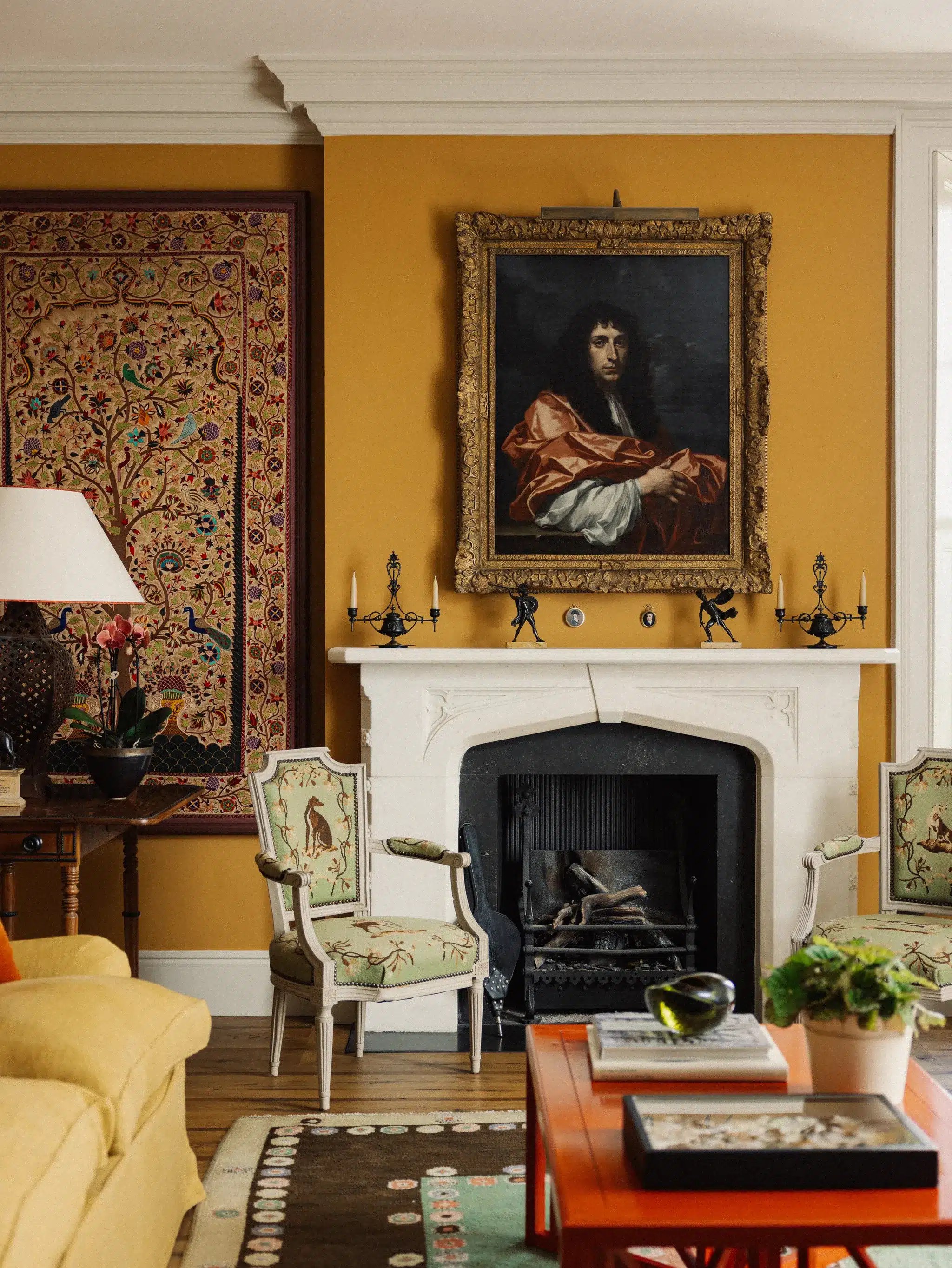 A colorful living room filled with patterned cushions, upholstered furniture, bookshelves, framed artwork and traditional furnishings layered to create a cozy maximalist interior.