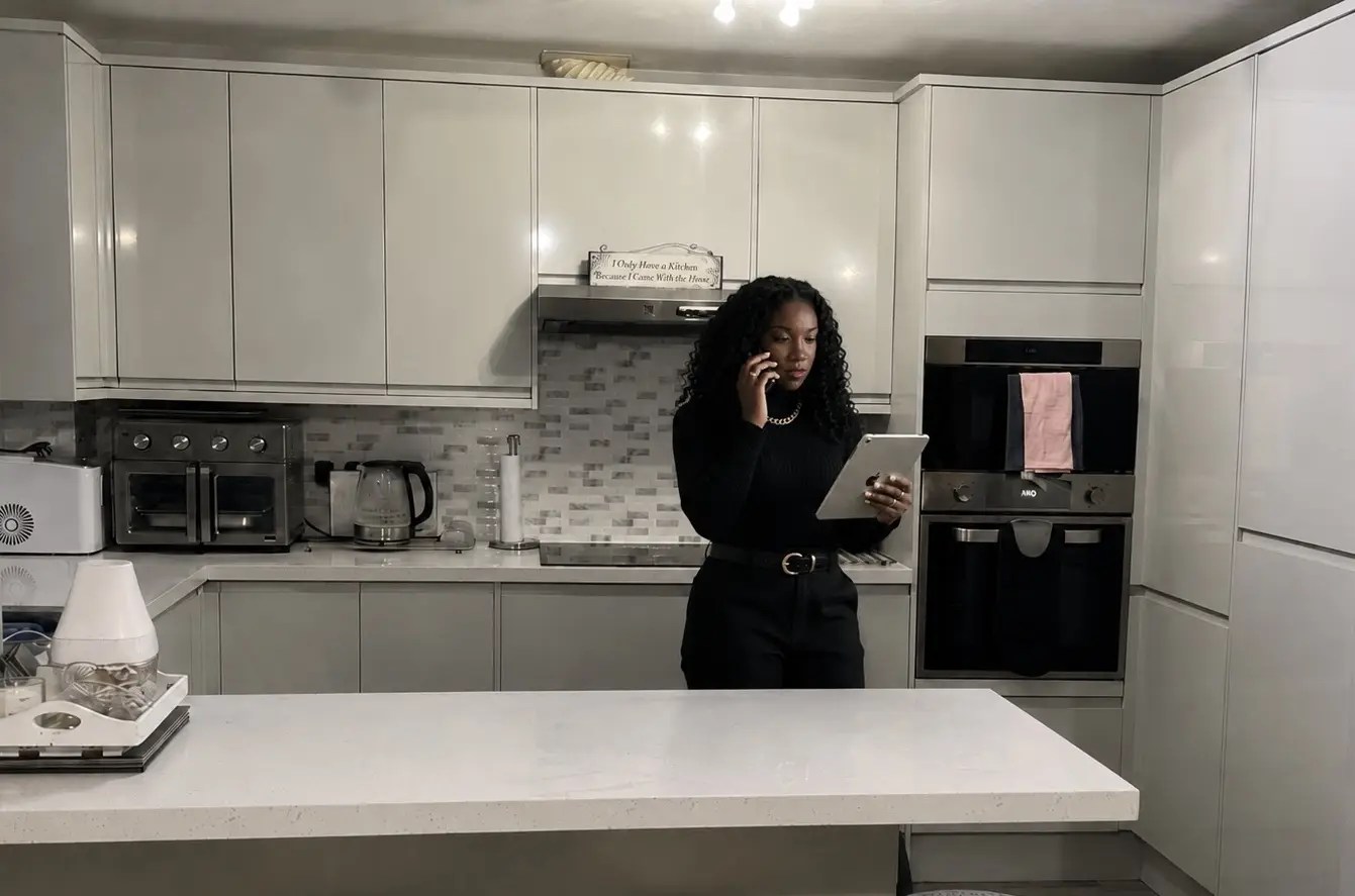 A Black woman using a tablet and phone in a modern grey-and-white kitchen, reflecting practical and stylish Home Wellness & Style.