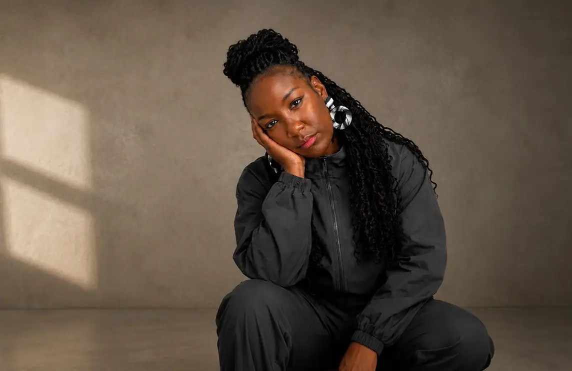Black British lifestyle blogger wearing a charcoal tracksuit in an editorial portrait with soft natural light and a minimalist neutral background, reflecting modern personal style and confidence