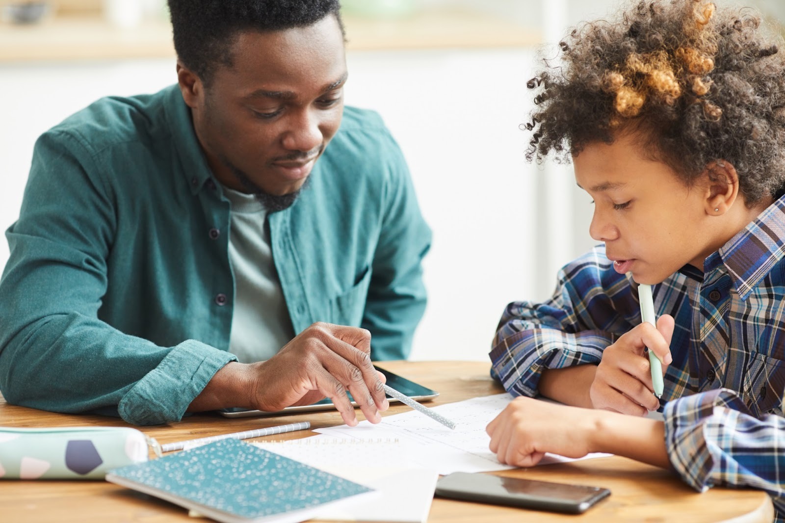 An educator and a student working together over a workbook at a table