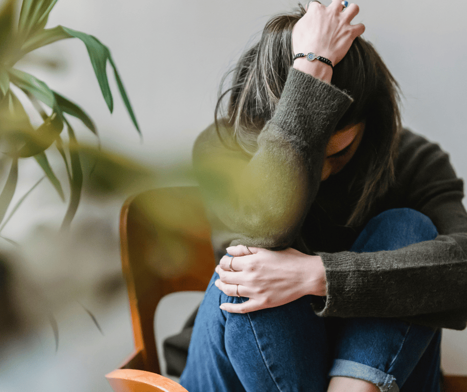 Woman sitting curled up with head in hand, expressing emotional pain and overwhelm after betrayal or trauma.
