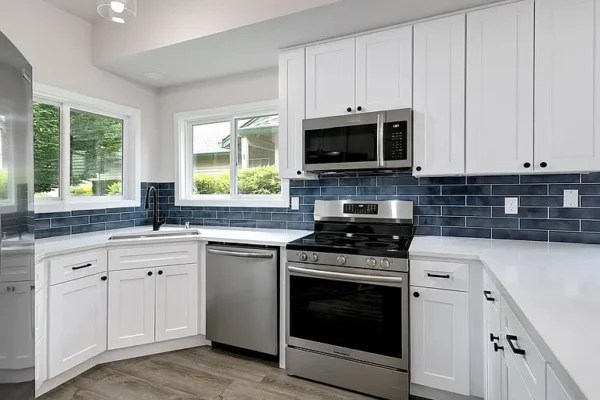 Kitchen remodel with white custom cabinets, stainless steel appliances, and navy blue subway tile backsplash.