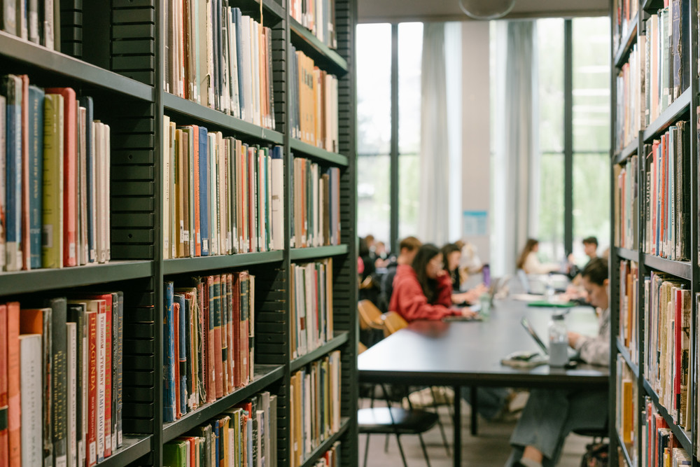 Library shelves with student sitting at desks in the background
