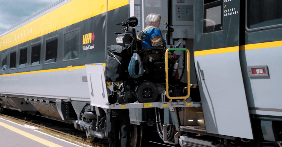 A wheelchair user boarding a VIA Rail train using a platform lift at a Canadian train station.