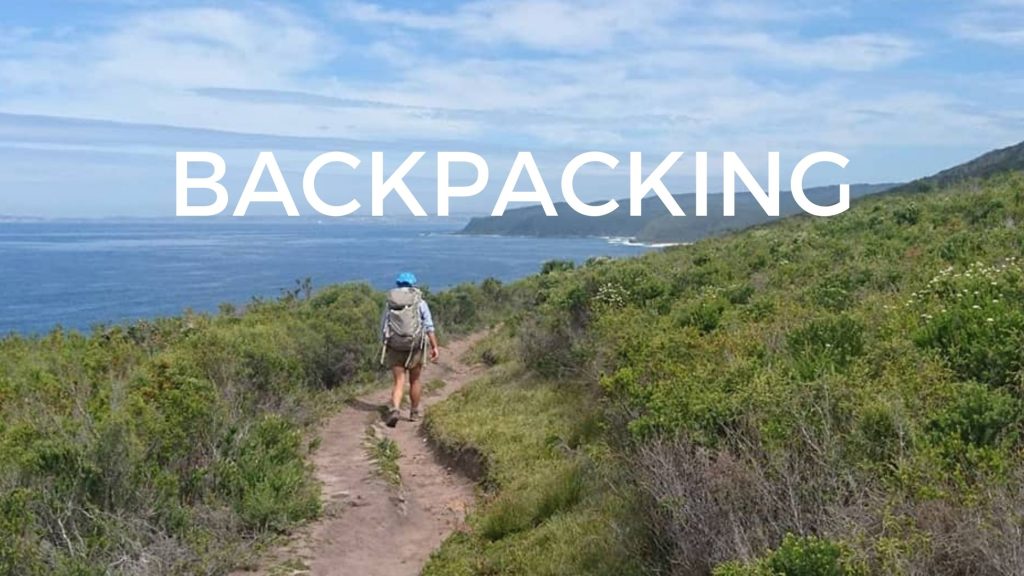 hiking with a backpack along a coastal dirt trail through green brush set above the coast