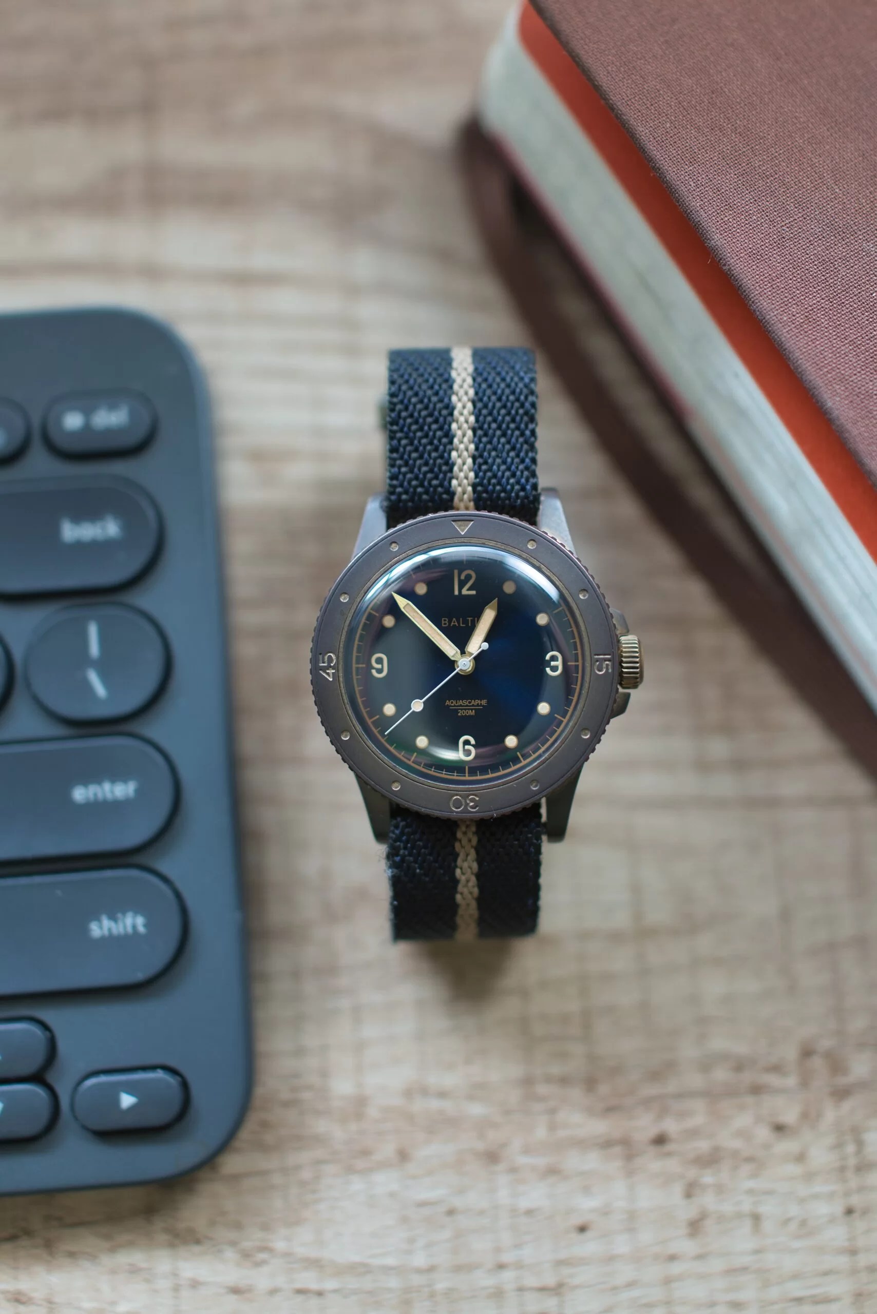 Aquascaphe Bronze on Blue/Harvest stripe Crown and Buckle Chevron Strap on wooden desk next to computer keyboard and brown Molskine journal