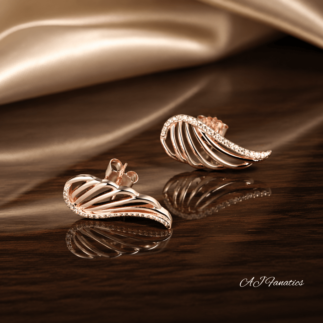 The Winged Adorners Statement Earrings featuring sculpted rose gold wing-shaped studs with openwork design and sparkling champagne gem accents.