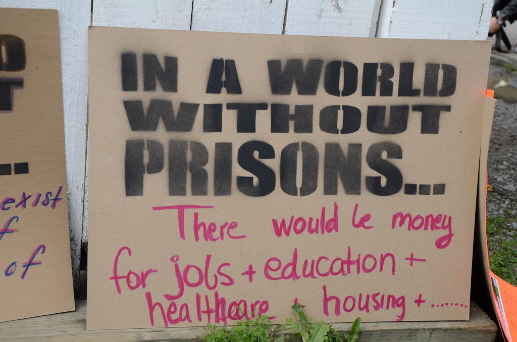 A photograph of a placard reading, 'In a world without prisons, there would be jobs and education and healthcare and housing