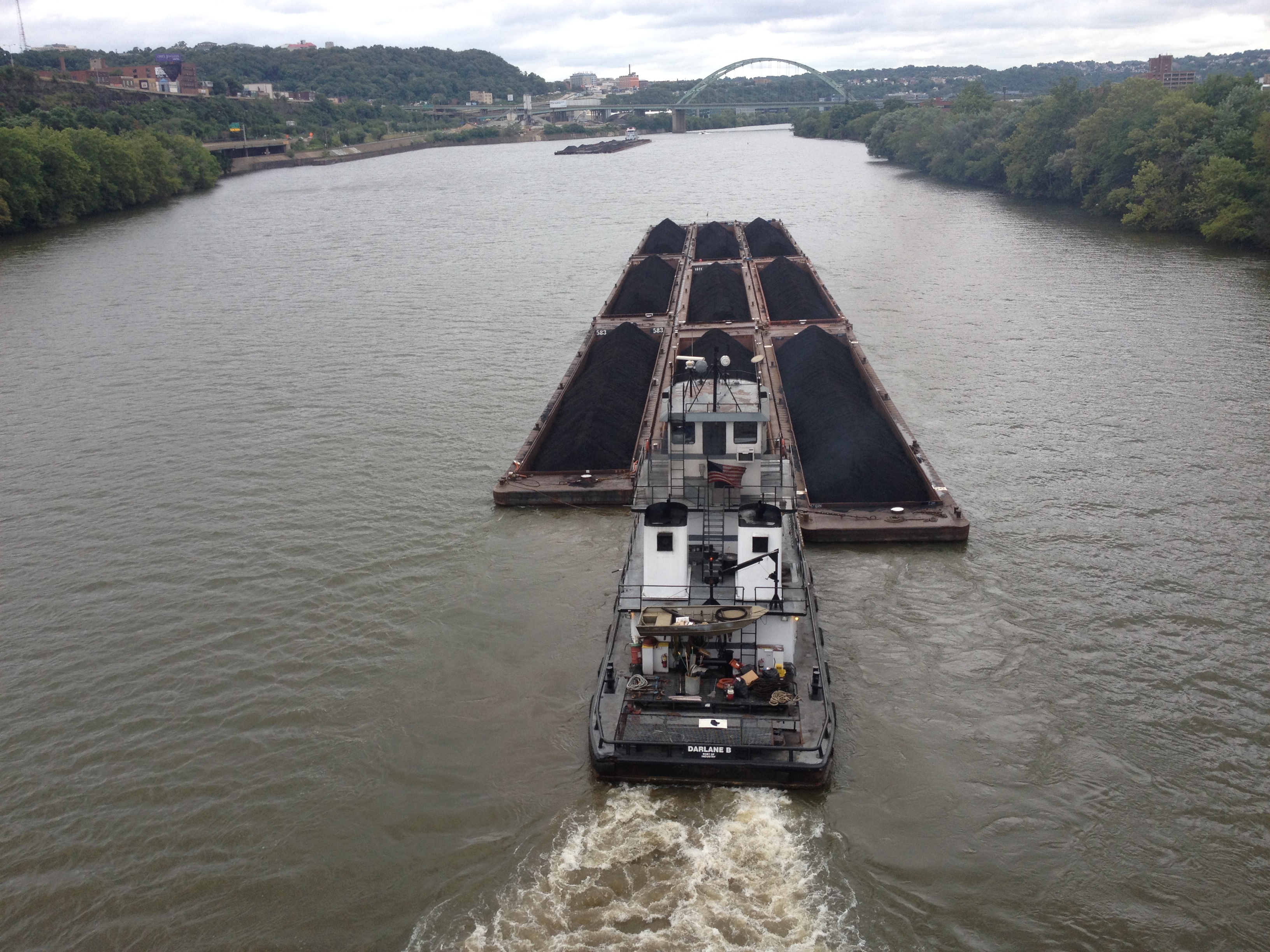 A tug boat pushes a barge full of coal up a river.