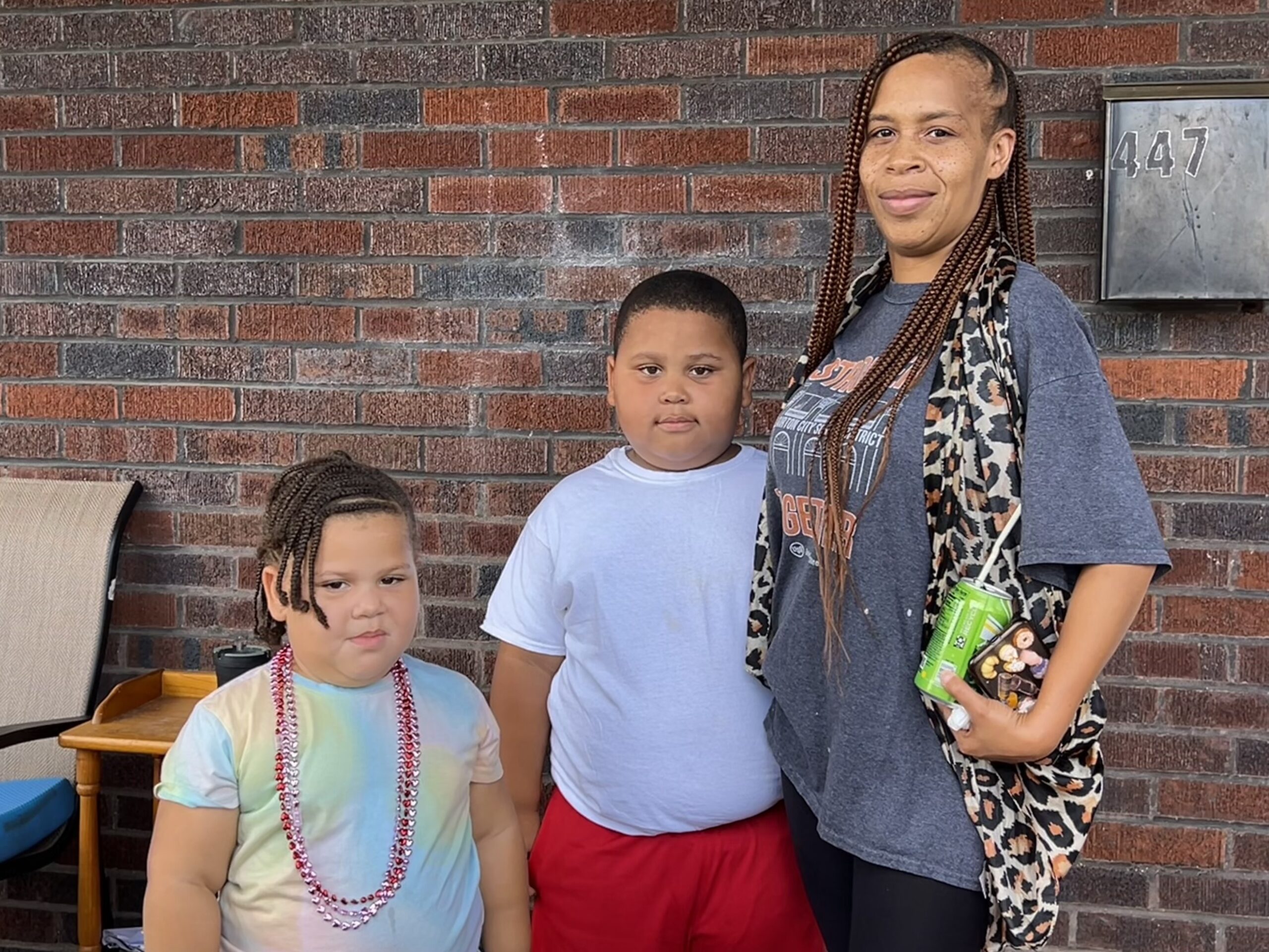A woman and two children stand in front of a brick building.