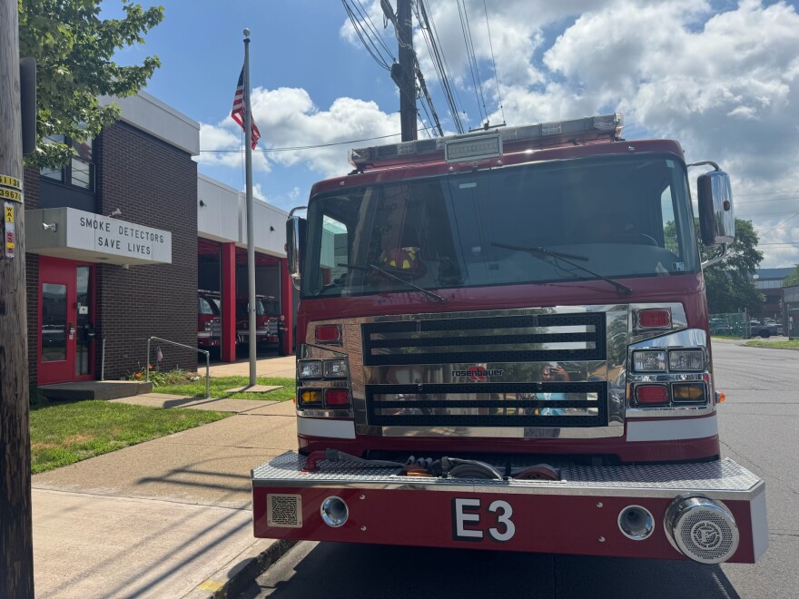 The front of a red fire truck in front of a fire station.