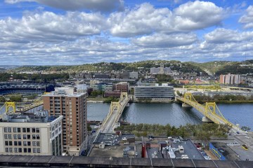 A downtown view of the Northside, across a river with two yellow bridges.