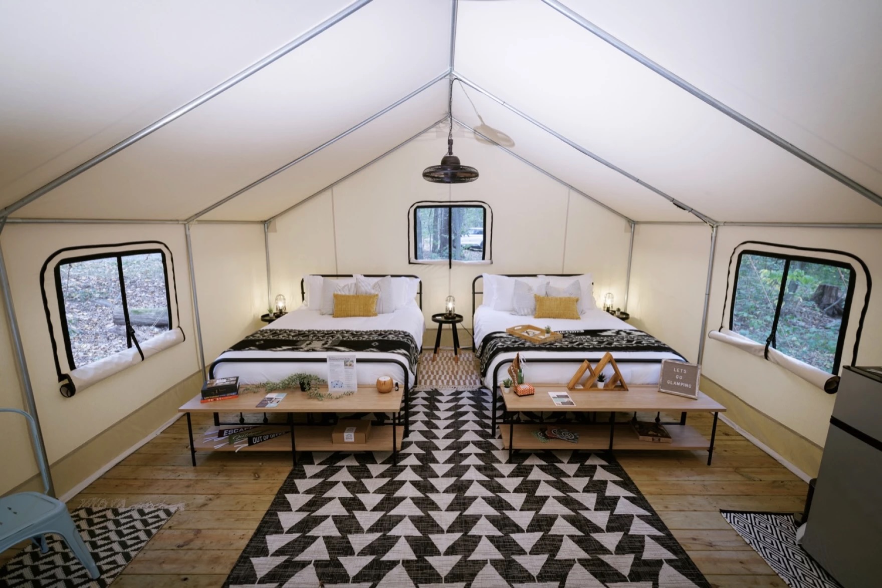 A large tent with a floor, three windows, two beds and a light fixture and carpet.